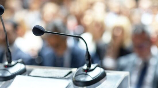 two microphones blurred audience shutterstock_2604940459